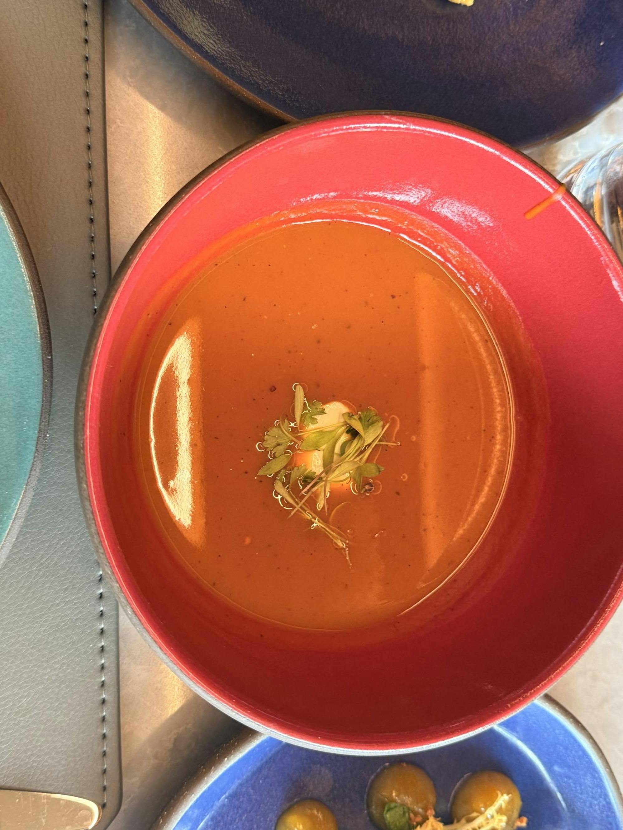 A reddish-orange soup served in a red bowl.