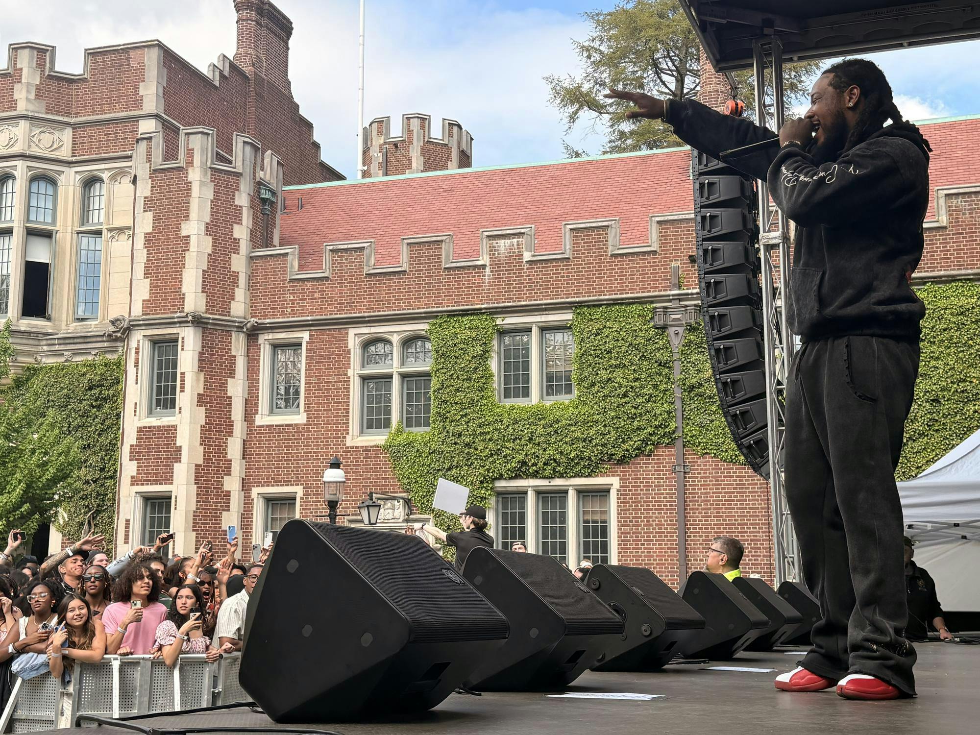 A man in a black hoodie and black pants performs in front of a student crowd. 