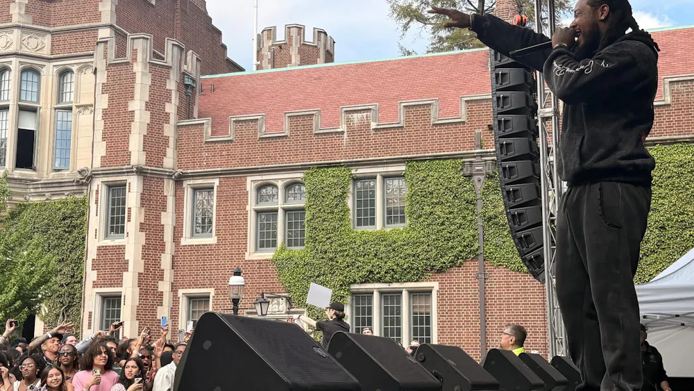 A man in a black hoodie and black pants performs in front of a student crowd.