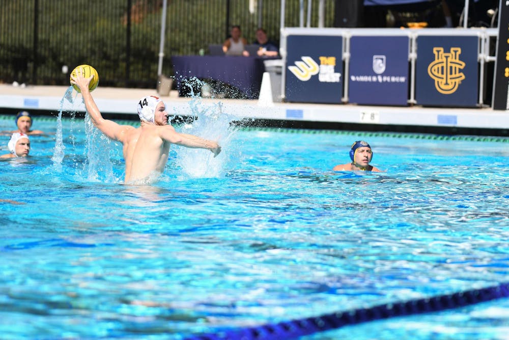 A man in the water eggbeating up preparing to shoot a water polo ball towards the goal while the other players in the water watch. 