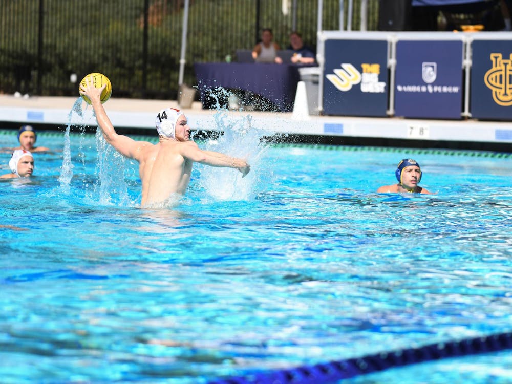 A man in the water eggbeating up preparing to shoot a water polo ball towards the goal while the other players in the water watch. 