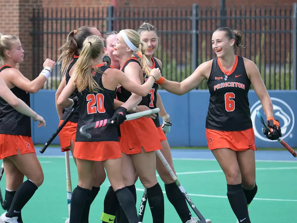 A group of women in black and orange jerseys smile and celebrate.