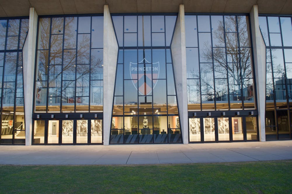 A large, glass building with the orange and black Princeton crest in the middle. Trees are reflected in the building's glass.