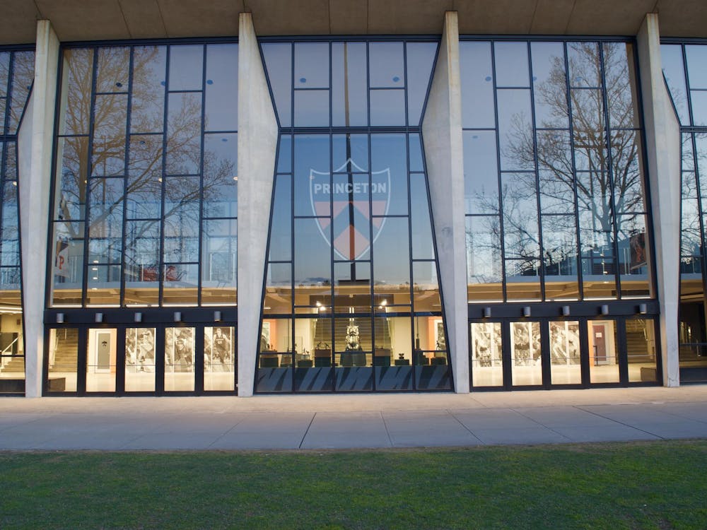 A large, glass building with the orange and black Princeton crest in the middle. Trees are reflected in the building's glass.