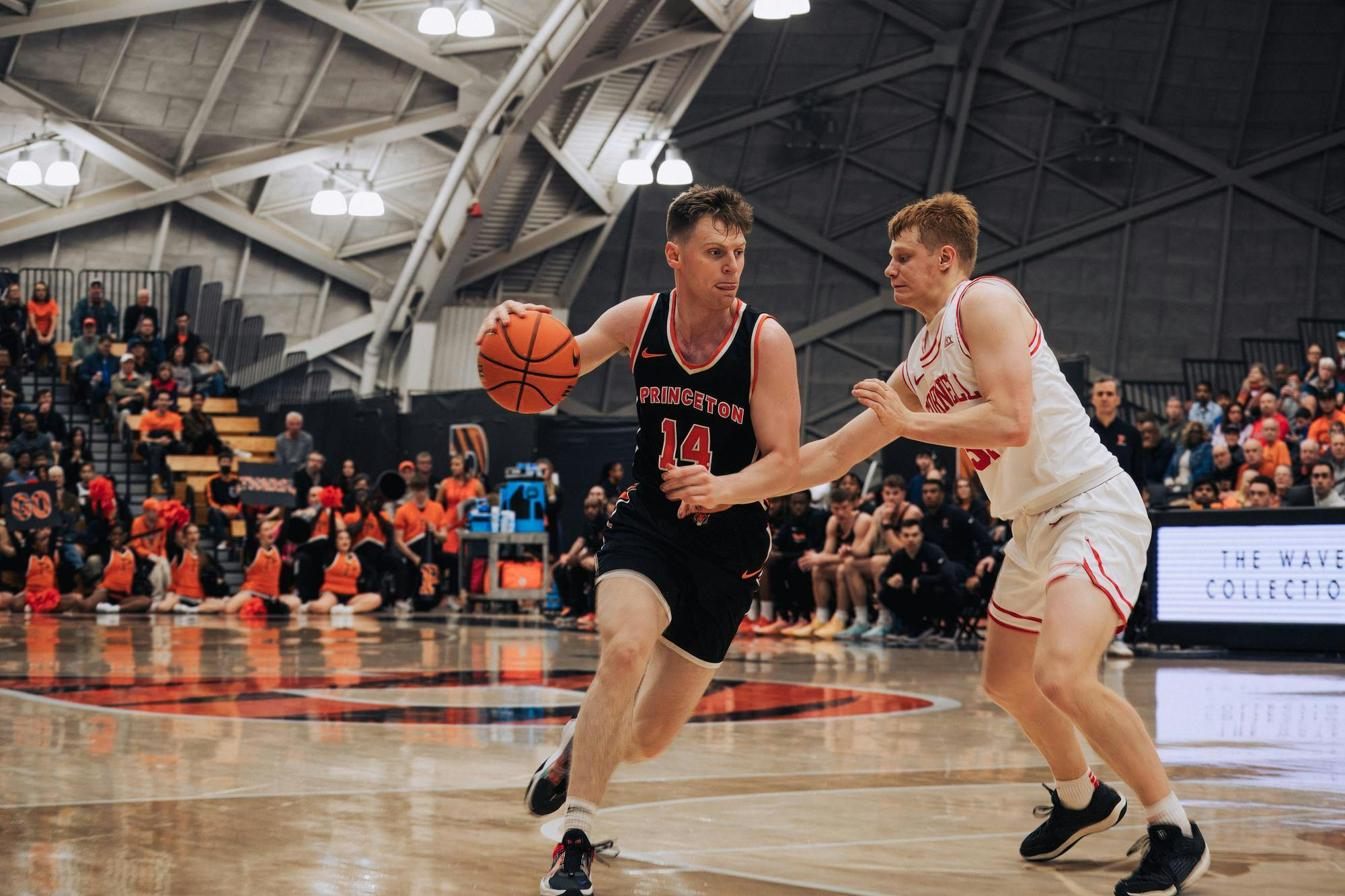 A man dribbling a ball on a basketball court with a defender attempting to guard him. 