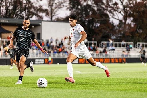 Man in white soccer jersey dribbles against man in black soccer jersey