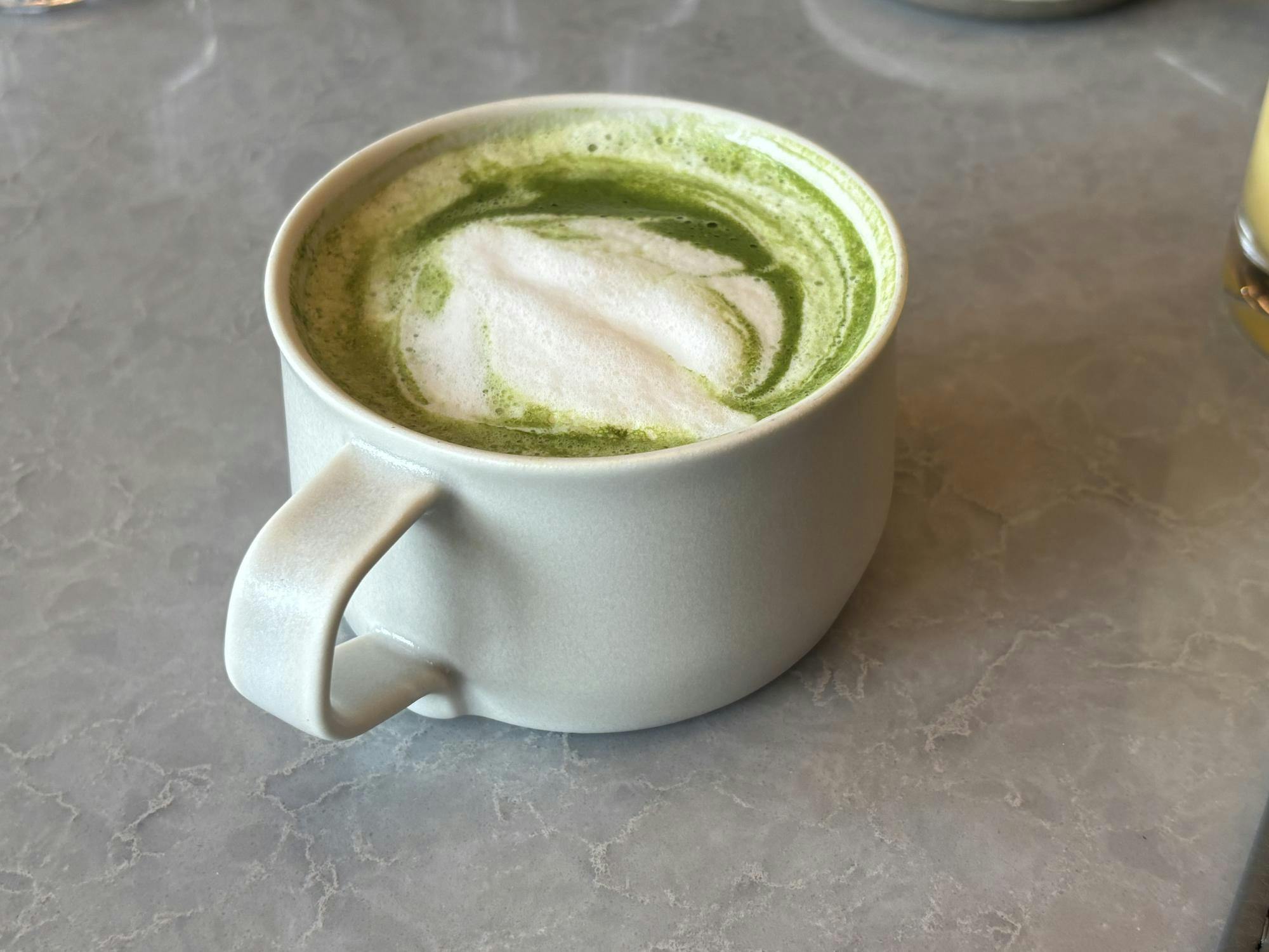 A green matcha latte with white foam swirls in a white mug.
