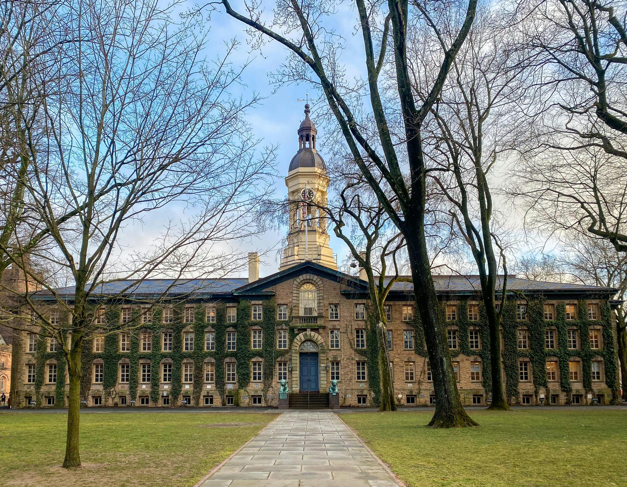 A ivy-covered colonial building stands in the background, with trees without leaves in the foreground.