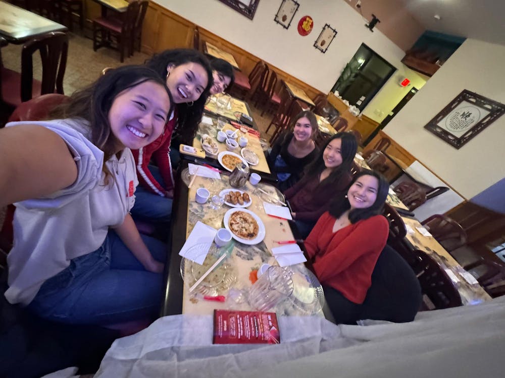 Six smiling girls sit at a table eating dim sum in a dimly-lit restaurant.