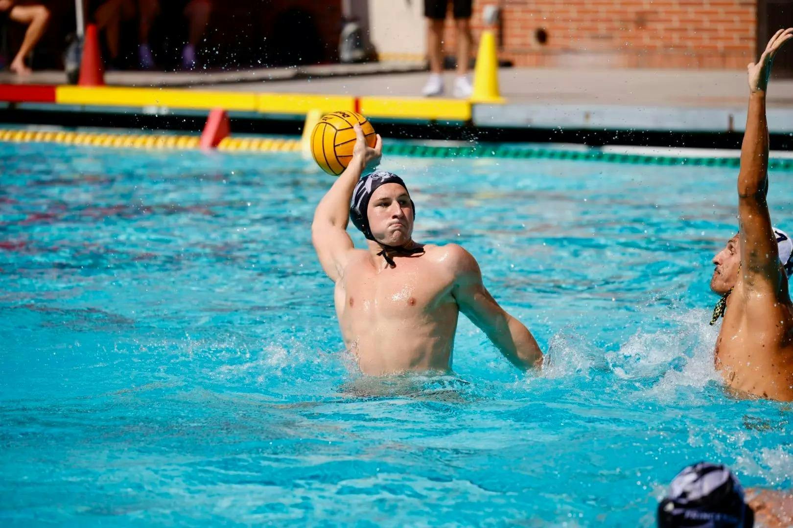 A man in the water wearing a dark cap getting ready to take a shot in an outdoor pool. 