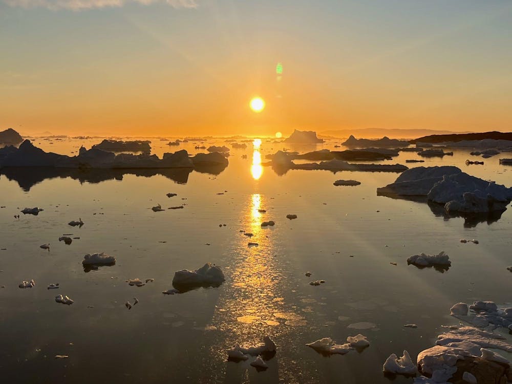 Photo of the sun in the center of the sky over a lake of glaciers and ice.