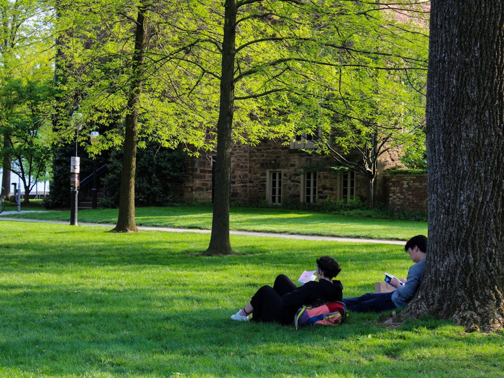 2 students laying down reading books against a tree in front of Nassau Hall.
