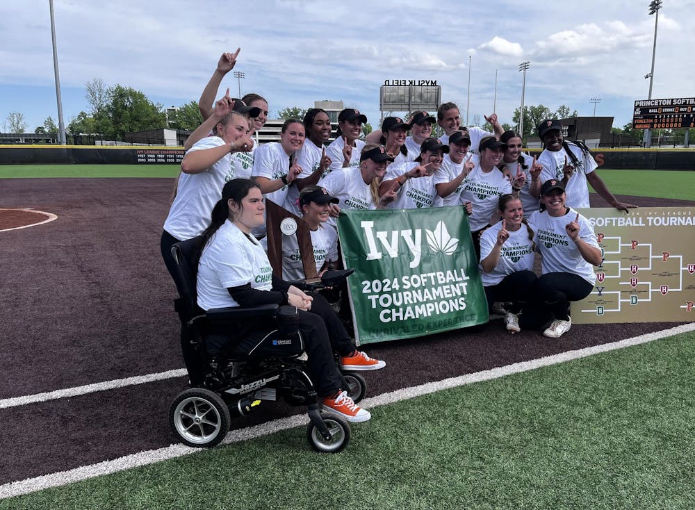 Group of about 16 softball players in white t-shirts that read "Ivy Tournament Champions" standing behind large green banner with the same wording.