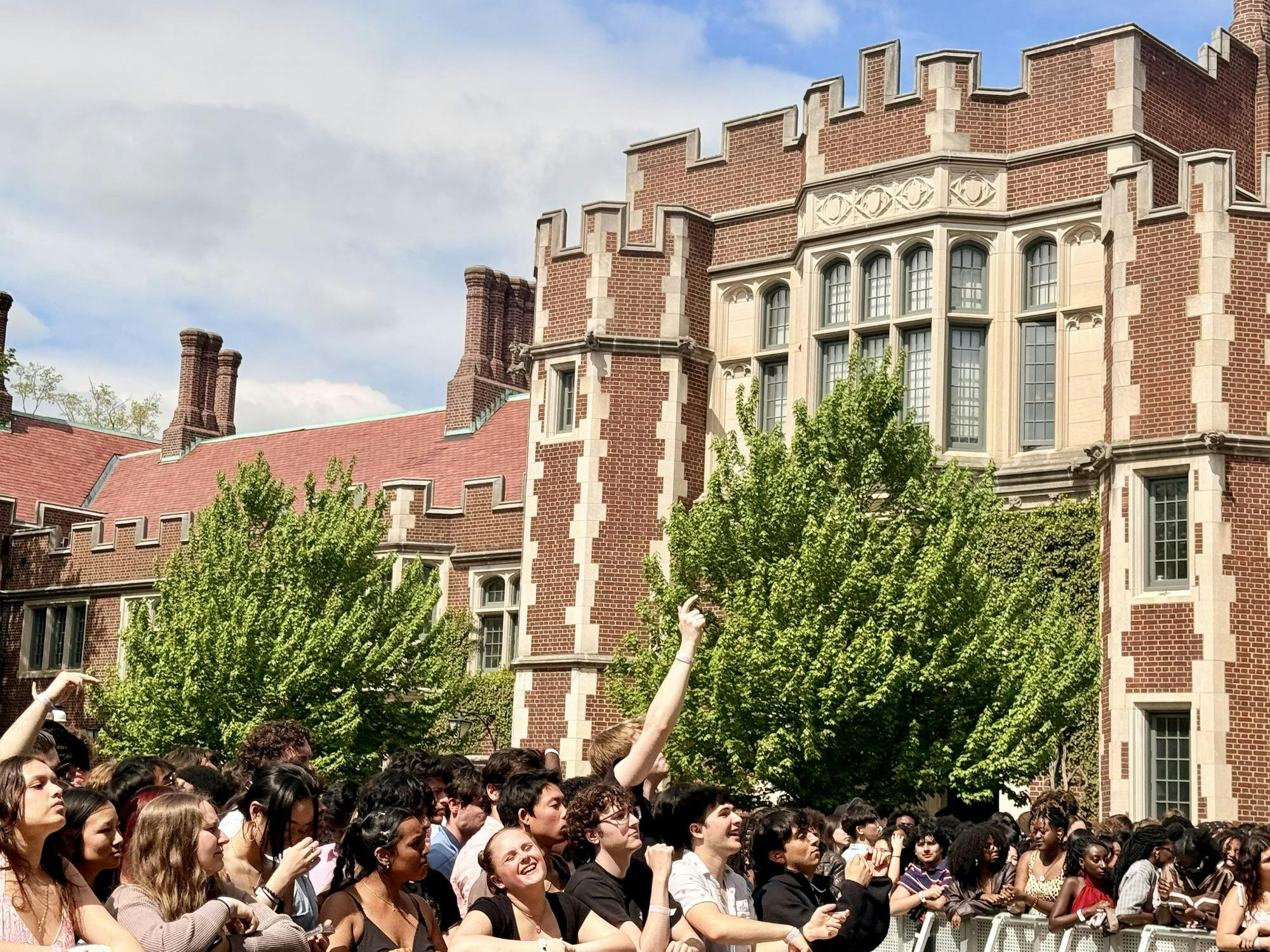 Crowd full of students behind a silver rail stand with a red brick building in the background. 