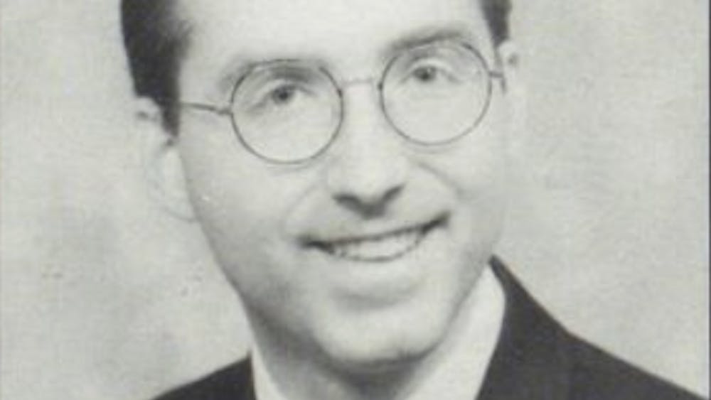 A black and white photo of a man in glasses smiling.