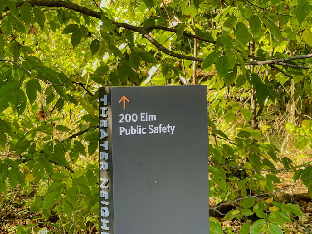 A sign surrounded by green foliage reads “200 Elm Public Safety” with an upward-pointing arrow.