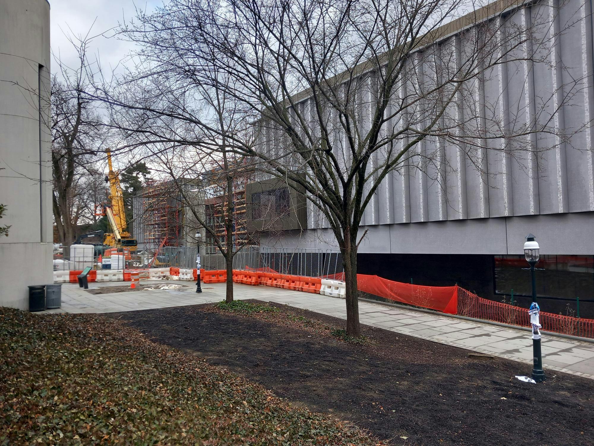 A large gray building with scaffolding is behind some trees.