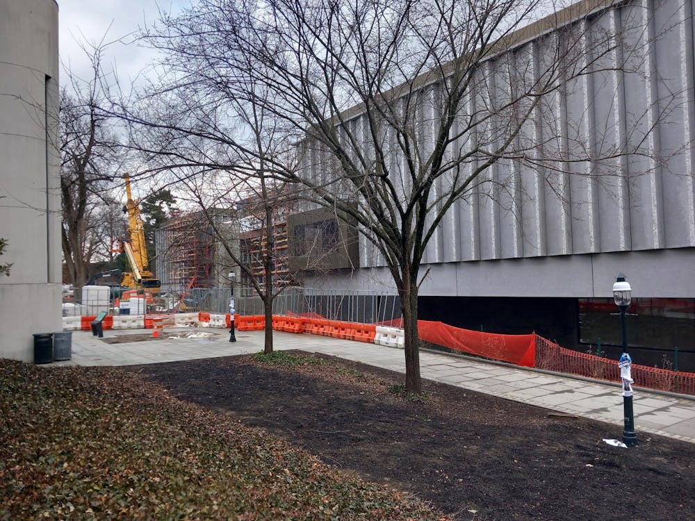 A large gray building with scaffolding is behind some trees.