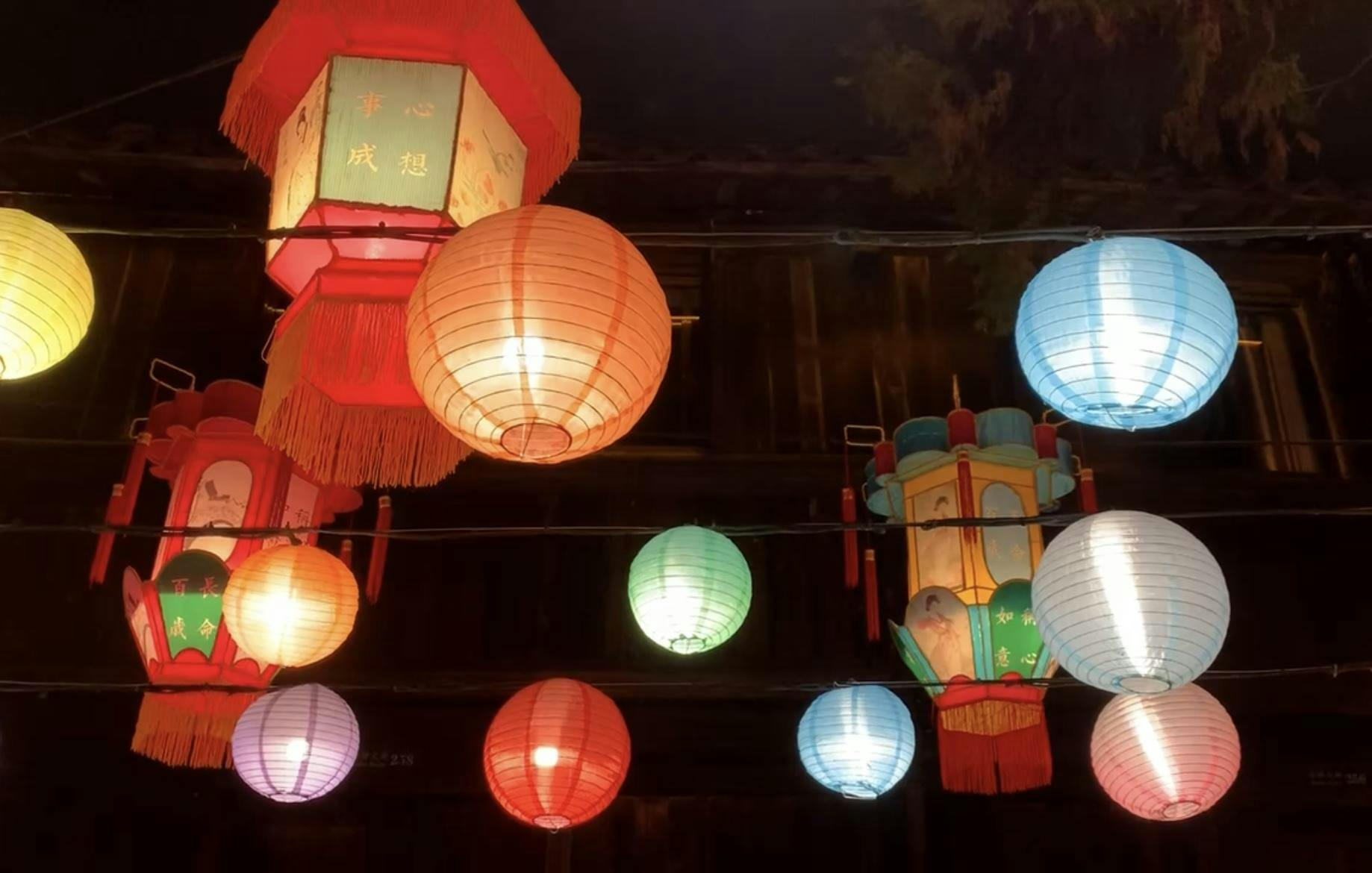 Several multicolored lanterns hanging from the ceiling. Three of the lanterns have lettering on them. 