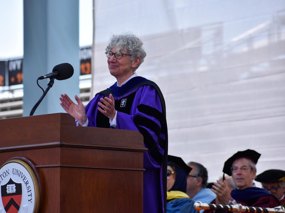 A woman in a purple graduation robe claps onstage behind a podium at a graduation ceremony. 