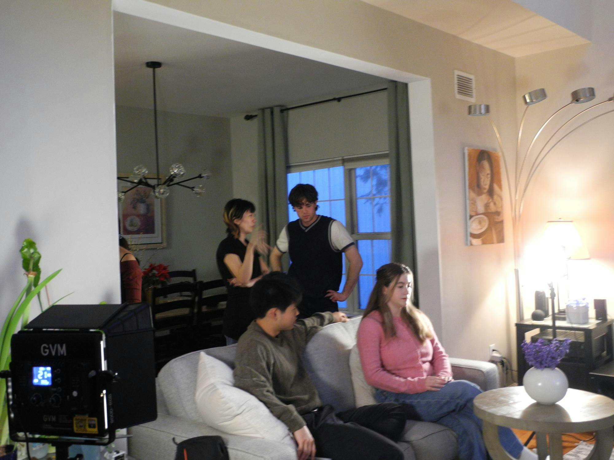 Four people in multicolored outfits. Two are sitting on a couch and two are standing behind the couch.