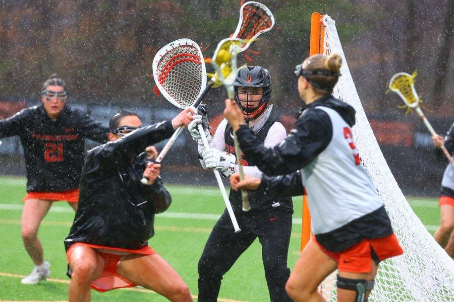 Princeton women's lacrosse in orange and black uniforms warm up on lacrosse field in rain, with lacrosse sticks waving in the air.  