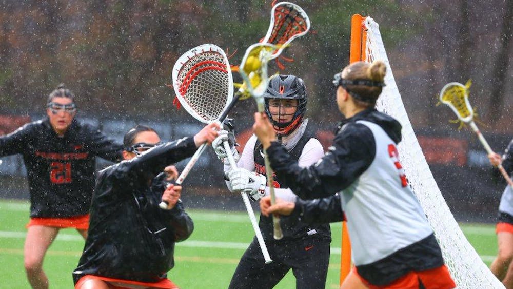 Princeton women's lacrosse in orange and black uniforms warm up on lacrosse field in rain, with lacrosse sticks waving in the air.  