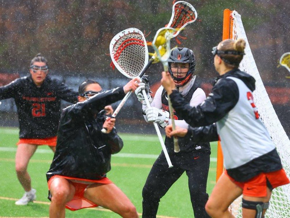Princeton women's lacrosse in orange and black uniforms warm up on lacrosse field in rain, with lacrosse sticks waving in the air.  