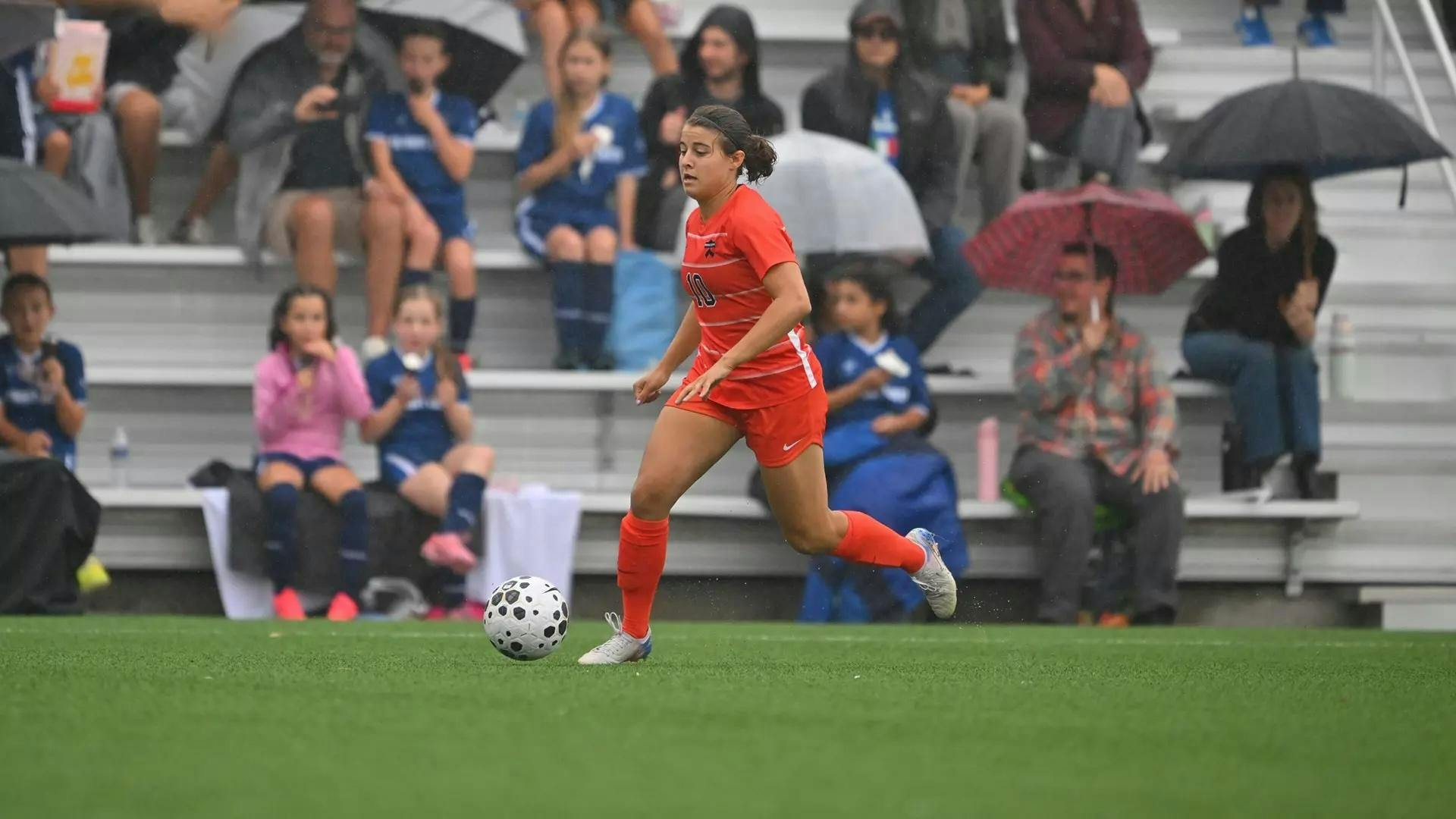 Player in orange dribbles a soccer ball on a green turf field.