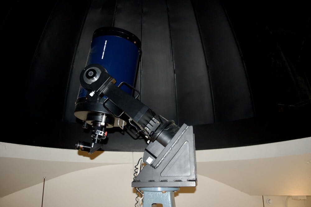 A navy blue telescope points toward the ceiling in an empty room. 