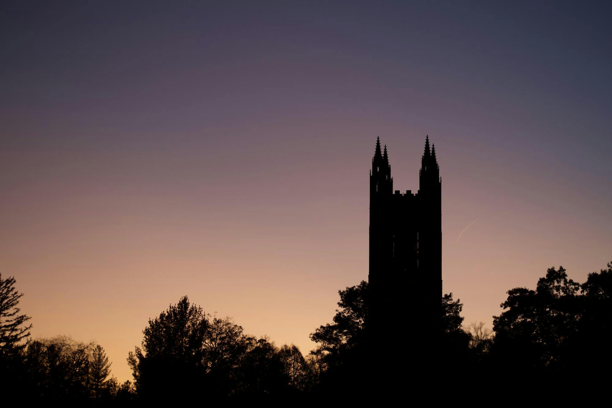The sun sets, with silhouettes of trees and a gothic tower present.