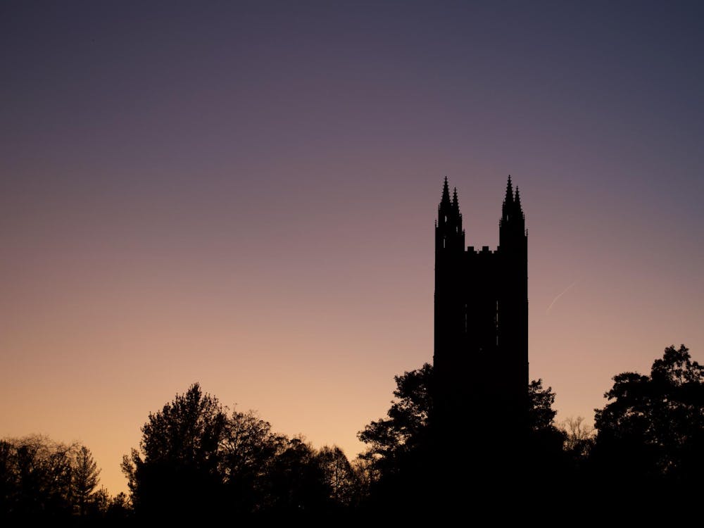 The sun sets, with silhouettes of trees and a gothic tower present.