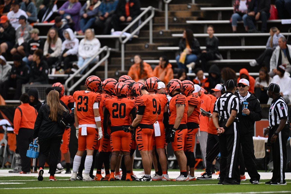 Men in football uniforms standing outside in a huddle.