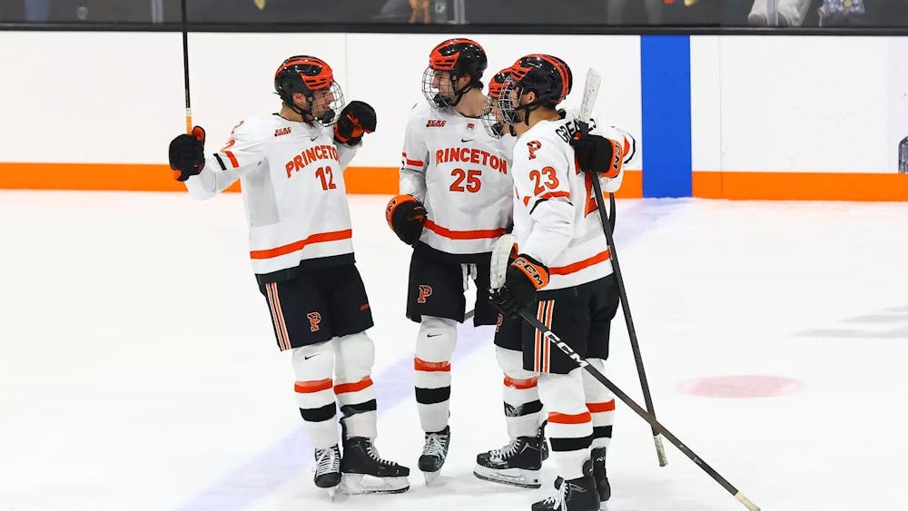 Three Princeton hockey players in white jerseys stand in a circle.
