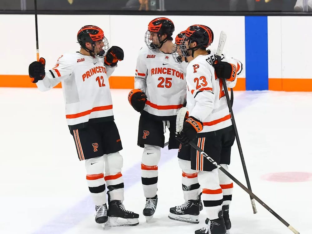 Three Princeton hockey players in white jerseys stand in a circle.