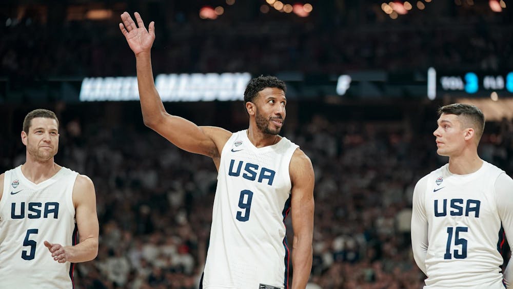 Man in white U.S.A. basketball jersey waves to crowd.