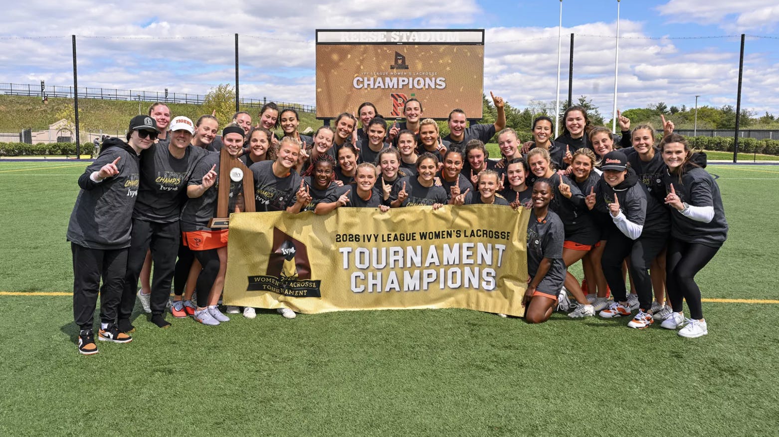 Players and staff hold up a “1” signifying first place and pose with a banner and trophy.