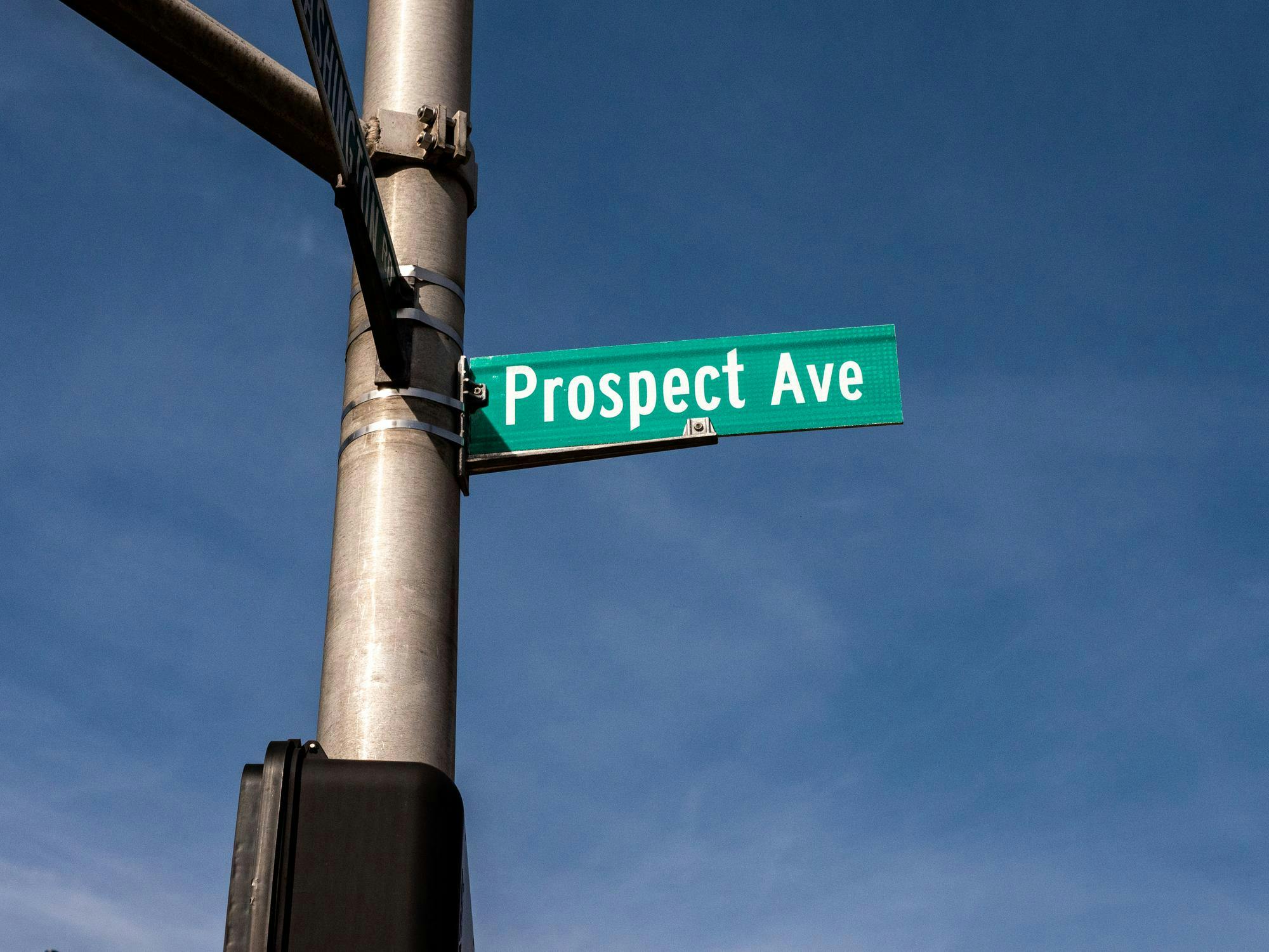 Green street sign against blue sky. The sign reads “Prospect Ave.”