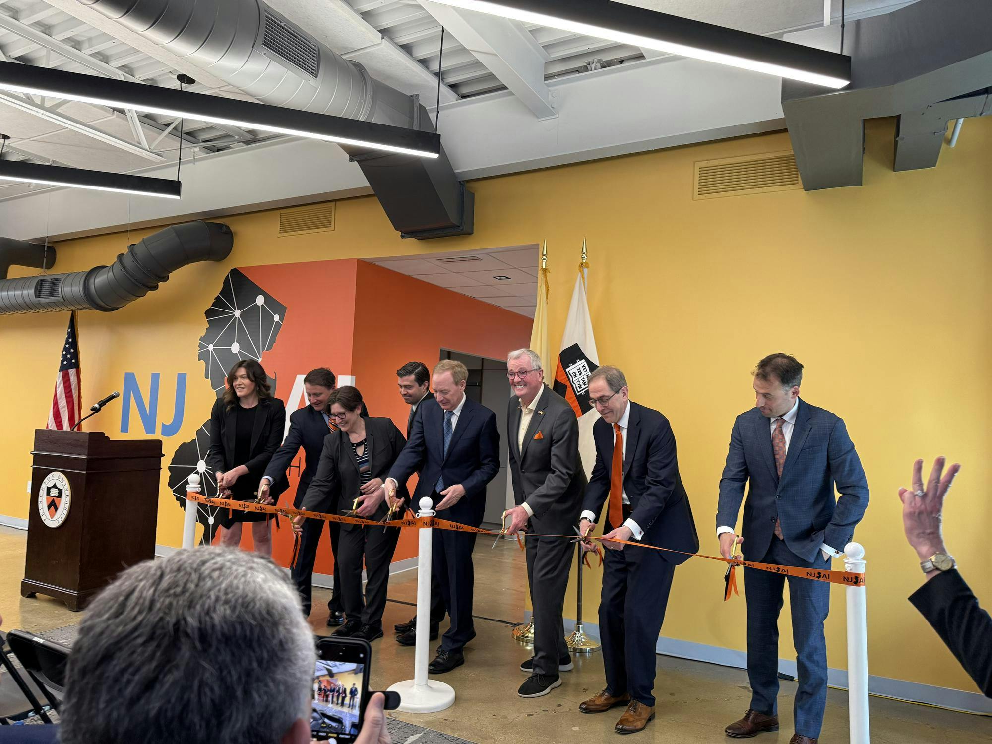 Eight people cut the ribbon in a yellow-walled building.