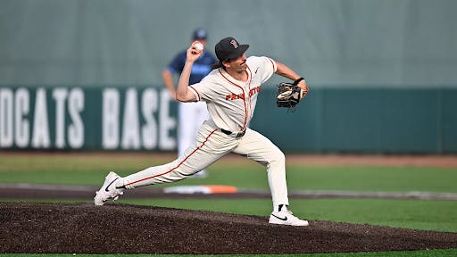Man in white and orange jersey pitches from a baseball mound.