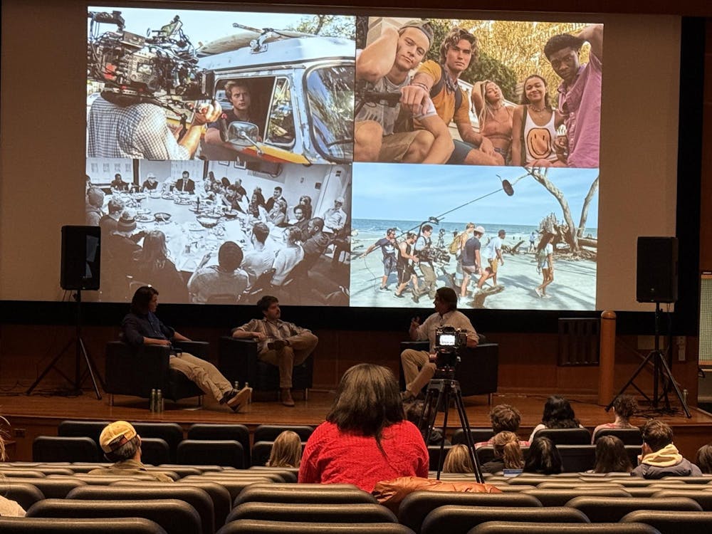Three men sit together in chairs behind a projected image of the cast of “Outer Banks.”