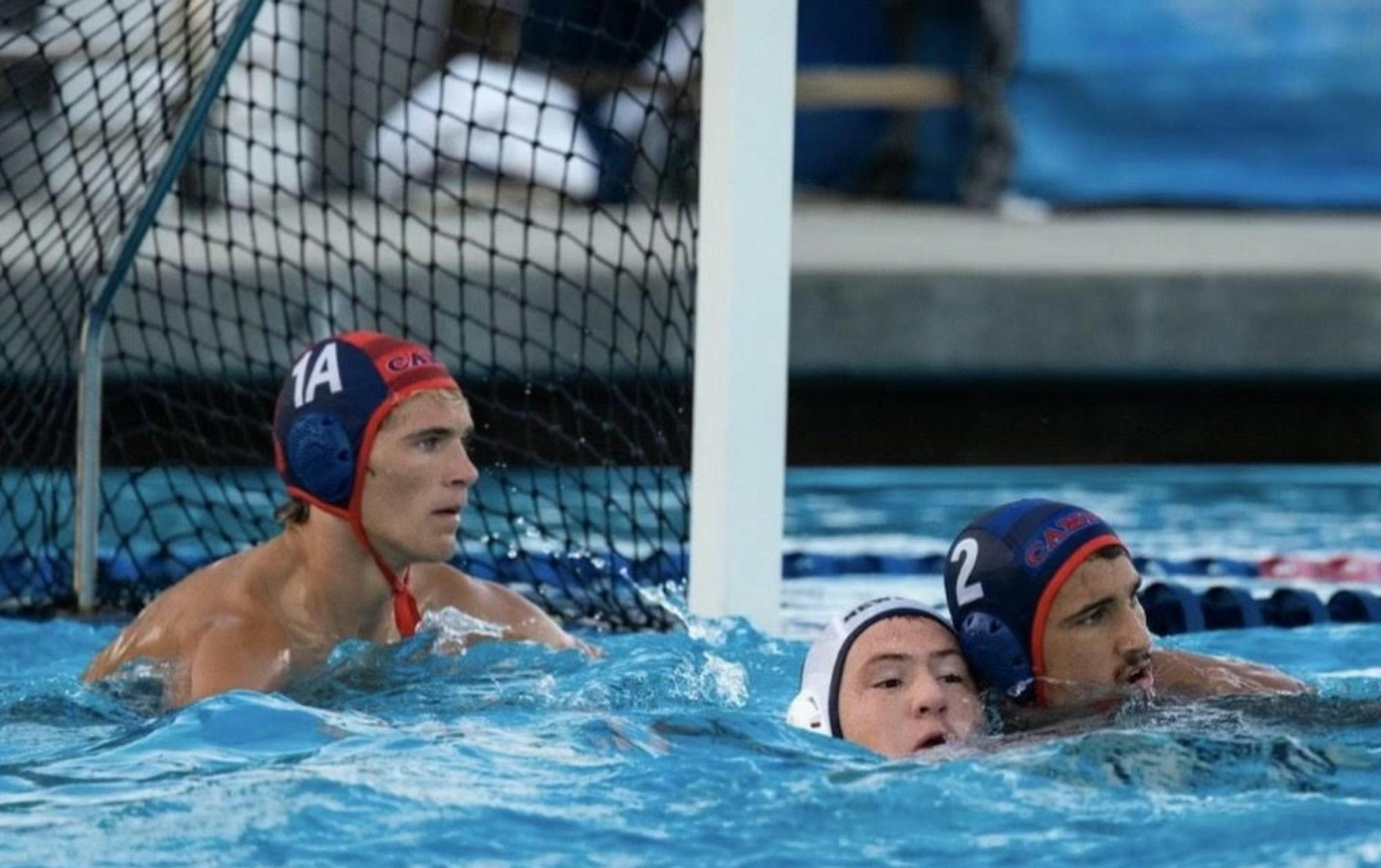 A man wearing a blue cap in the goal in the water waiting for a shot.