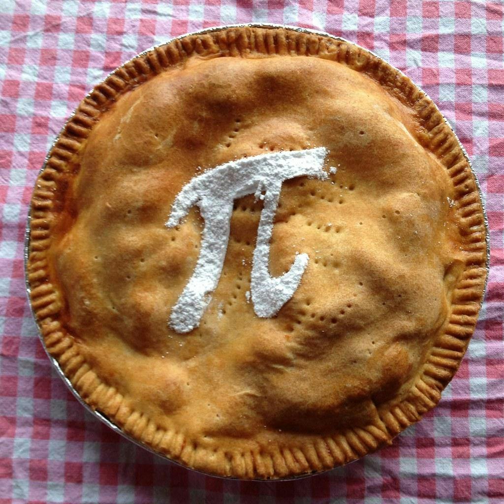 A golden circular pie with pinched crust on top of a red and white gingham background. In the middle of the pie, there is a white pi symbol that appears to be made of powdered sugar. 