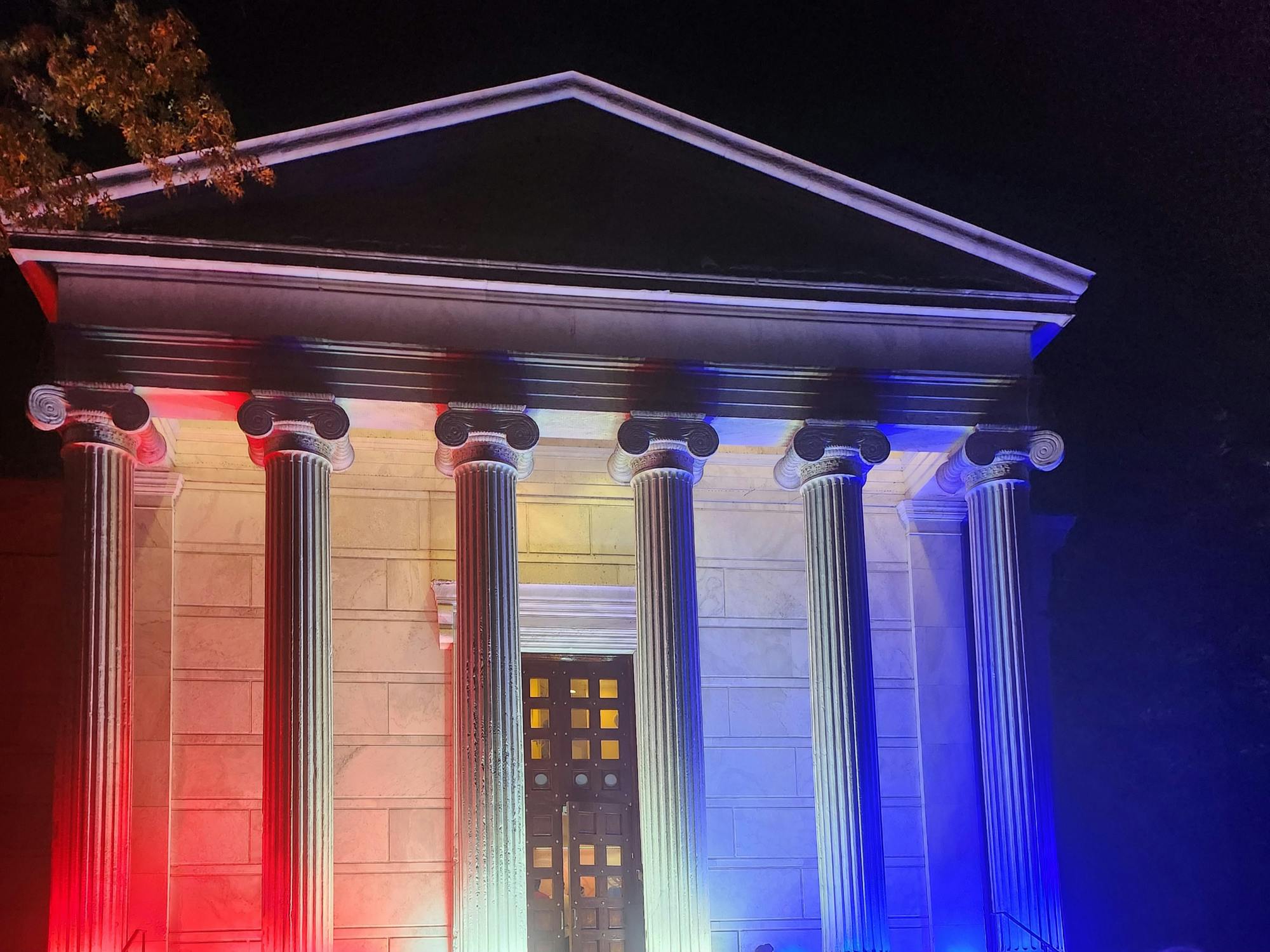 Red and blue lights shine on a white neoclassical building with columns.