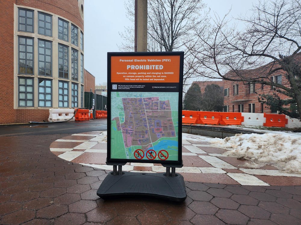 In the foreground, a sign shows the restricted area for scooters on campus. In the background, a brick building with construction stands. 