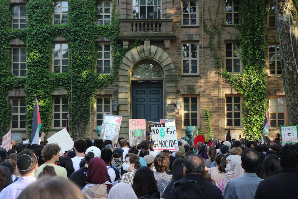 Protesters holding signs gather in front of a gray stone building with green vines.