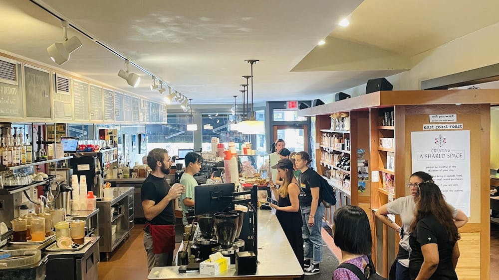 Customers line up to order coffee in front of a wooden shelf lined with coffee merchandise, while baristas prepare drinks.