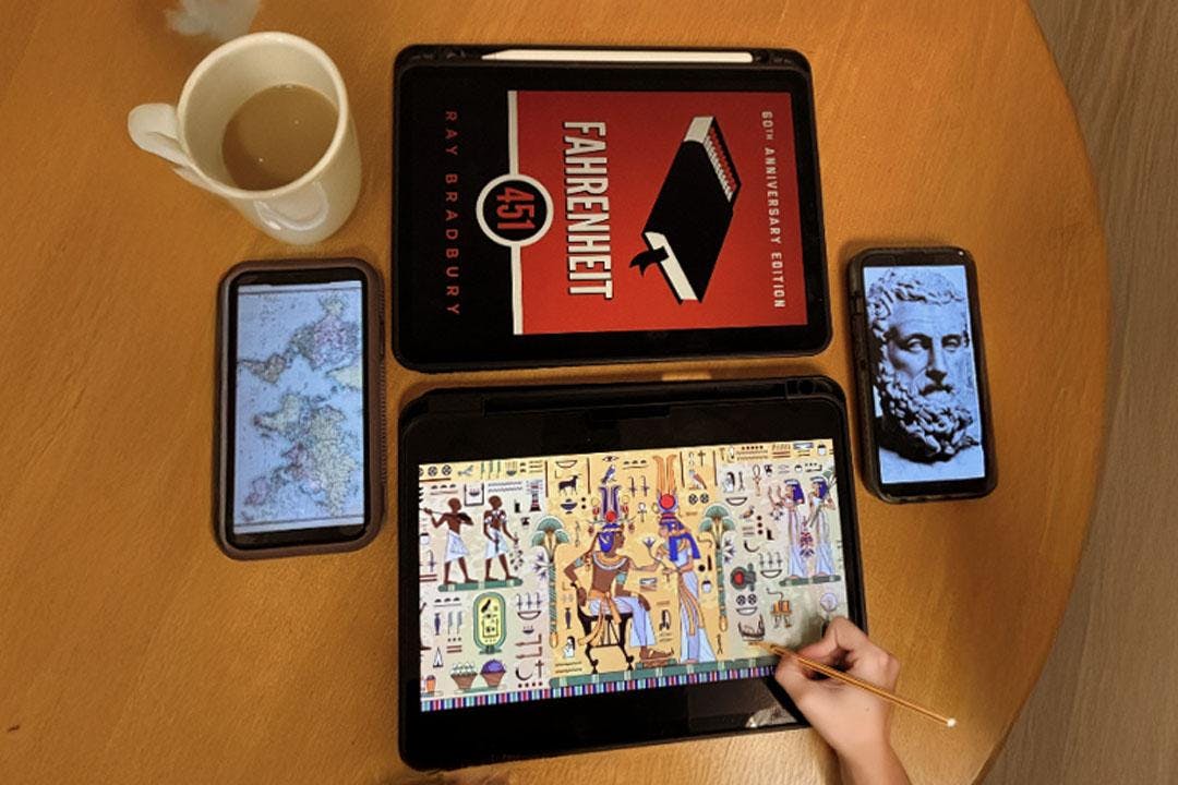 Images of Aristotle, Egyptian hieroglyphs, the cover of Fahrenheit 451, and a map are on the screens of devices on a wooden table.