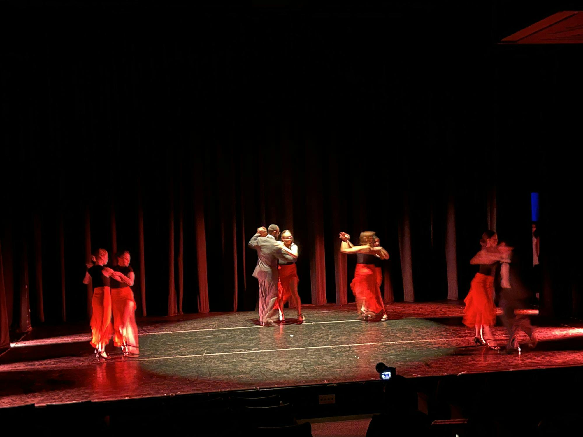 Four pairs of dancers on a dark stage illuminated by a spotlight on center stage.
