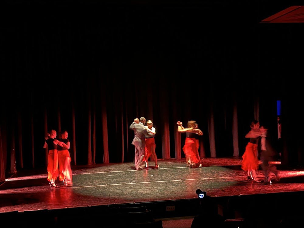 Four pairs of dancers on a dark stage illuminated by a spotlight on center stage.